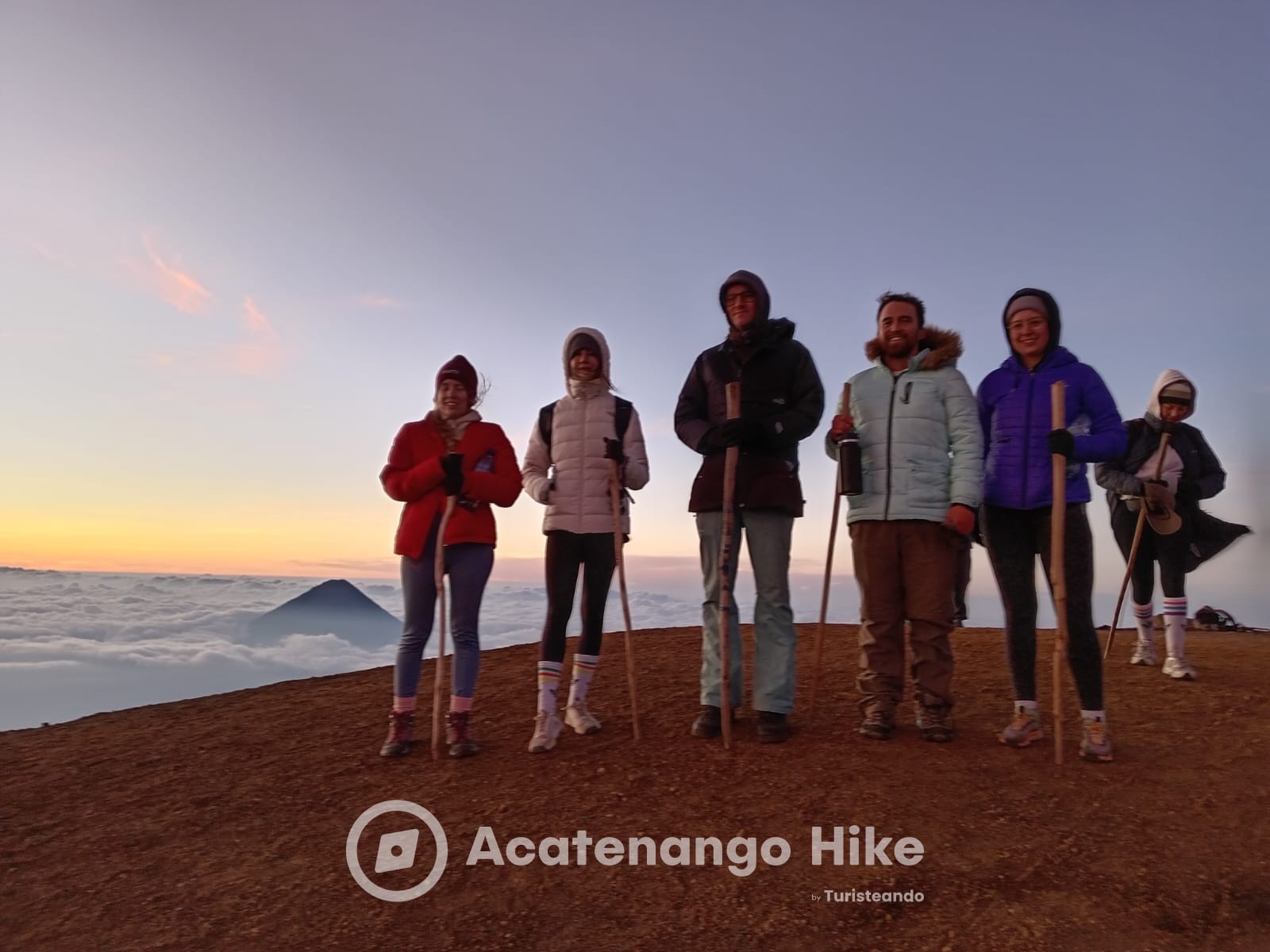 Hikers at the Acatenango summit at sunrise with Agua Volcano above the clouds
