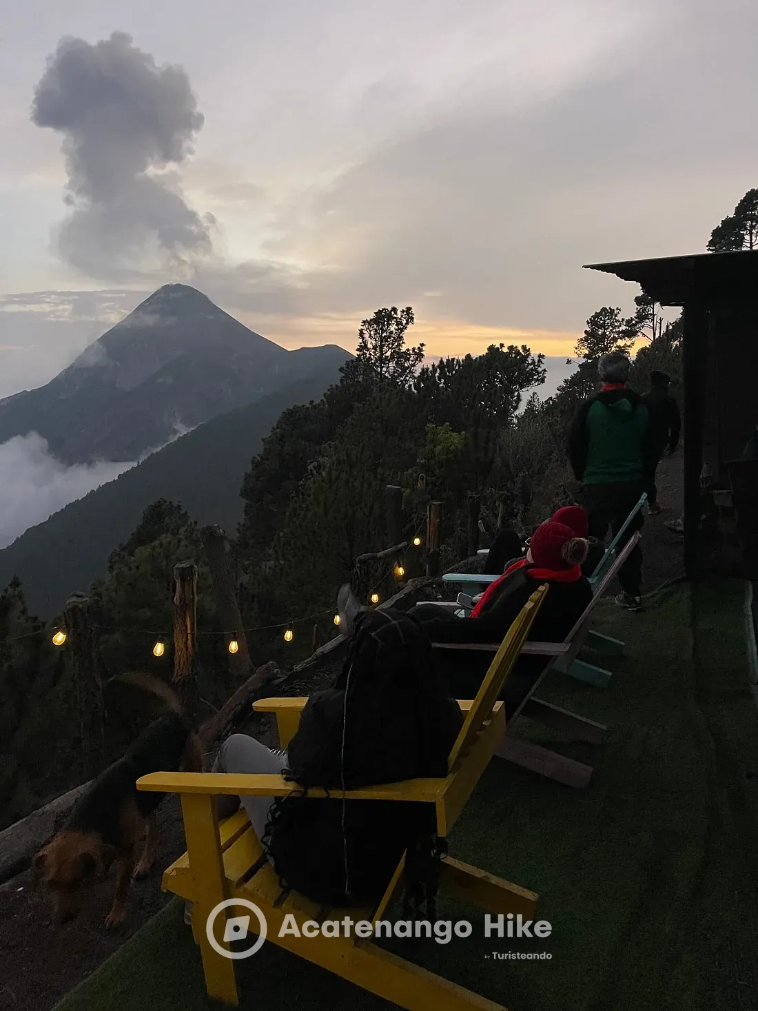 Travelers relaxing on chairs at the Acatenango base camp at dusk, facing Volcán de Fuego