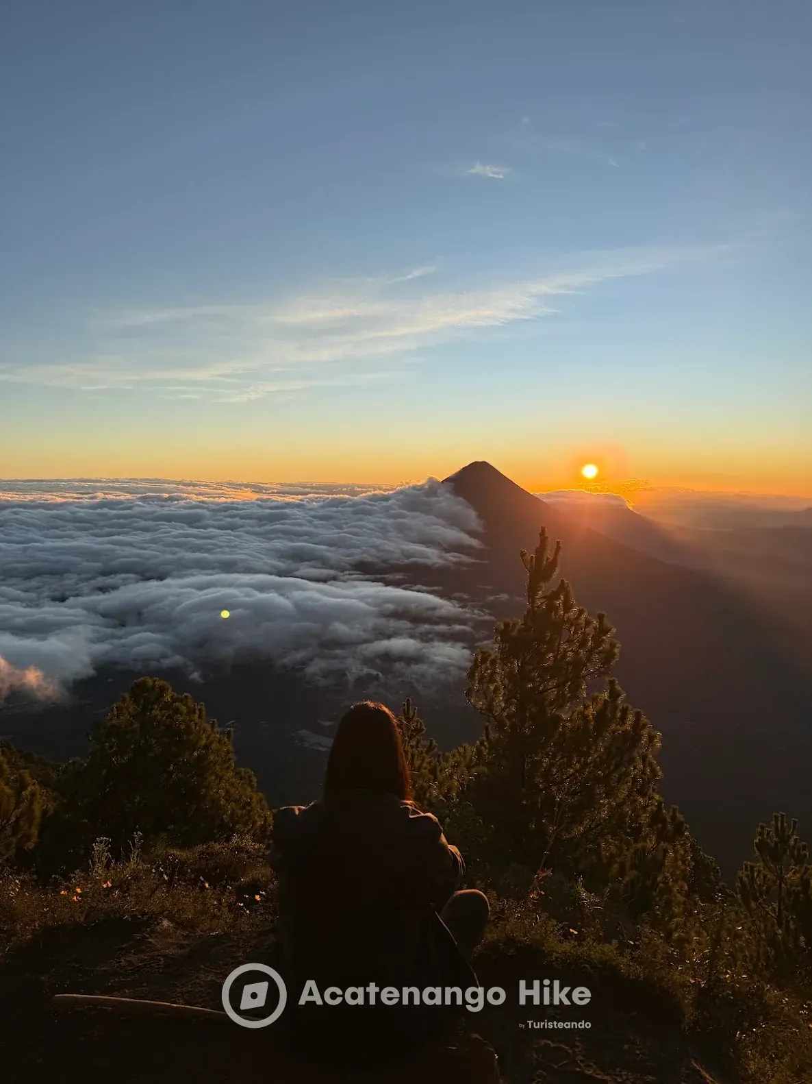 Hiker watching the sunrise above the clouds from the Acatenango summit on the 4x4 sunrise tour