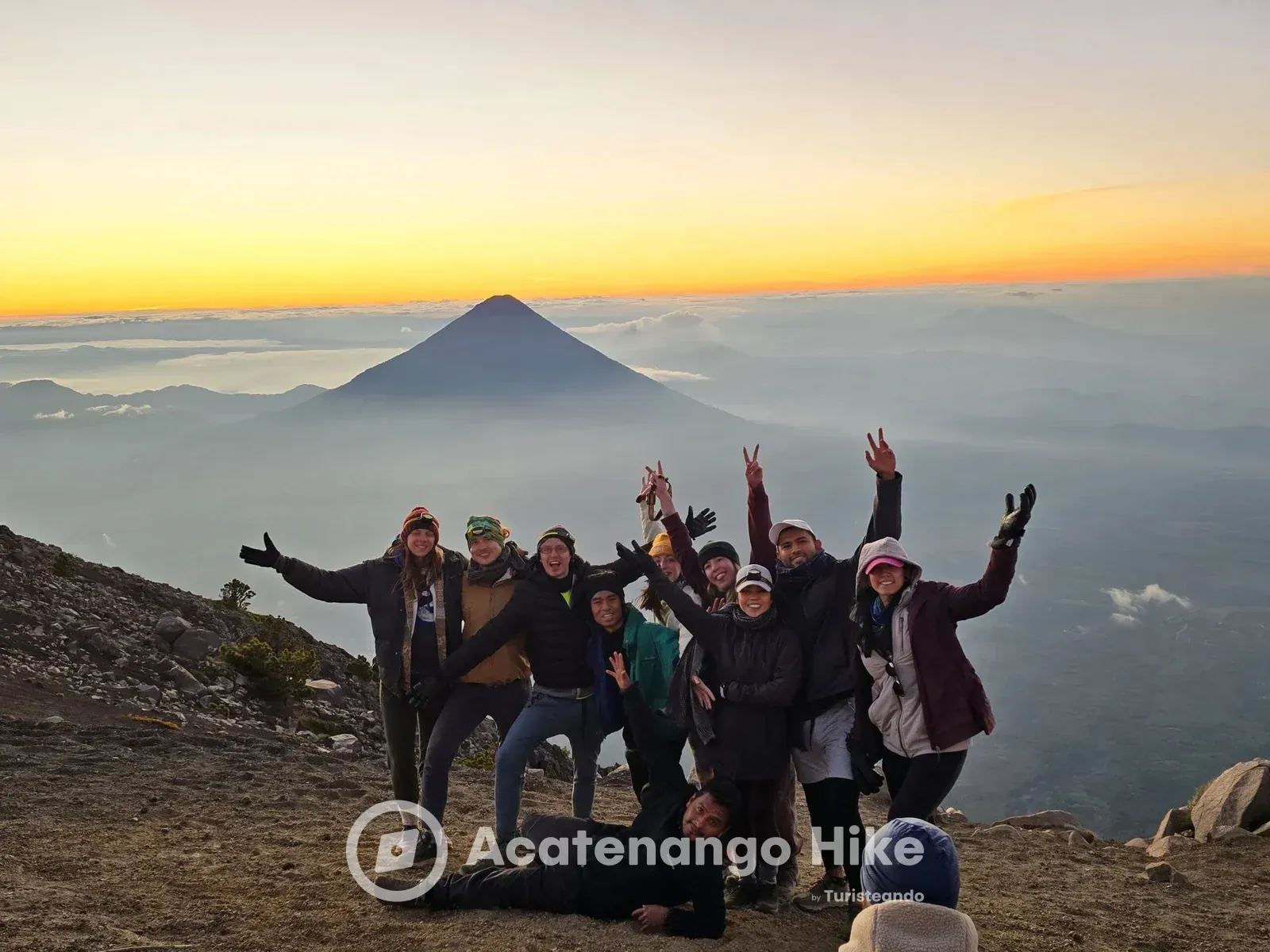 Group celebrating at the Acatenango summit at sunrise with Agua Volcano behind