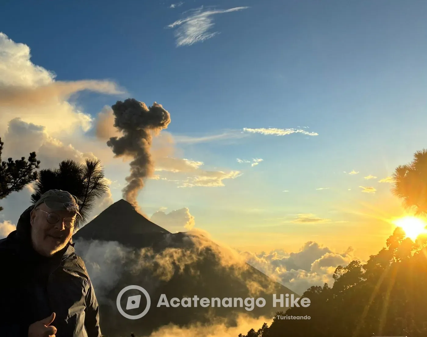 Caminhante no acampamento base do Acatenango enquanto o Vulcão de Fogo solta uma coluna de cinzas ao pôr do sol
